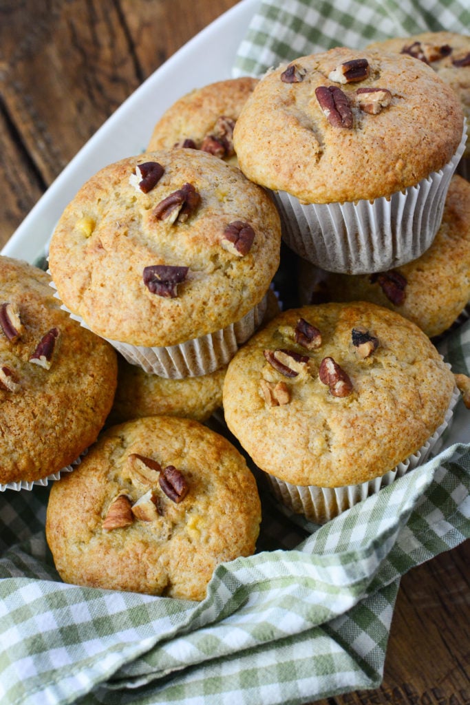 9 banana muffins with pecans sitting pretty on a white plate with green and white striped serving cloth.