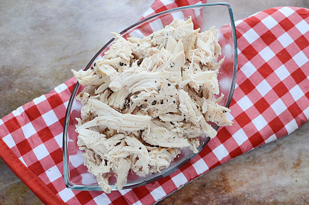 Slow cooked pulled chicken breast on a transparent breakable serving plate sitting on top of a red and white oven mitt