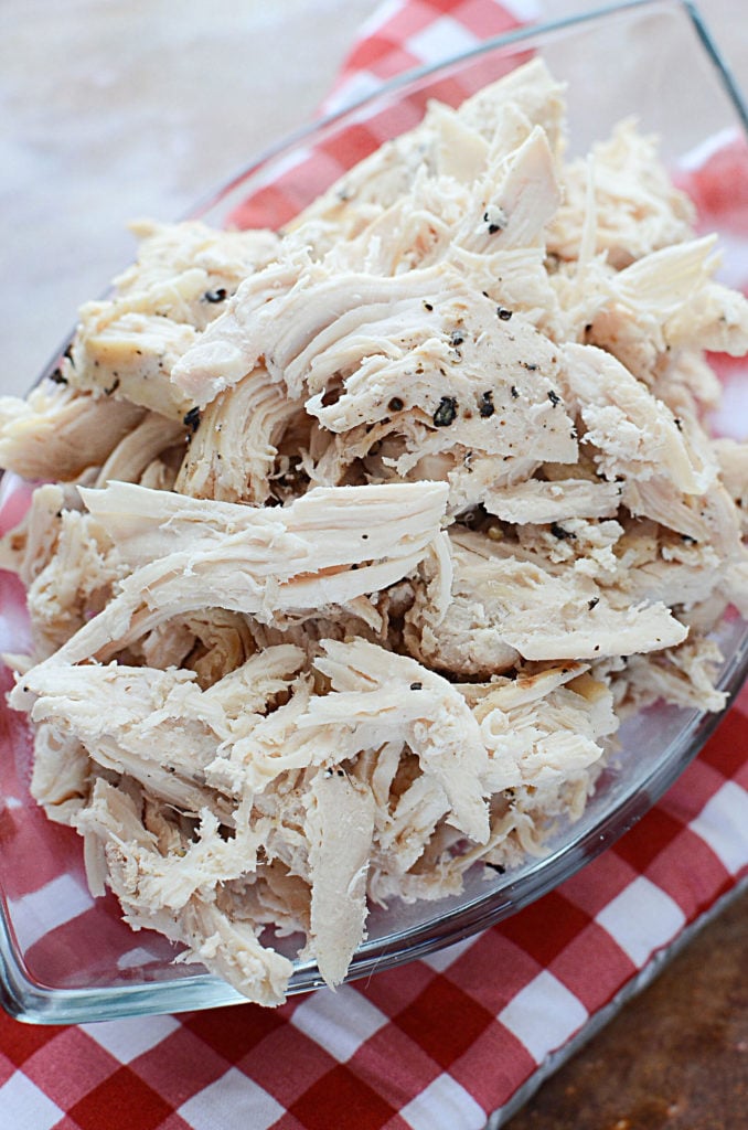 A close up image of Slow cooked pulled chicken breast on a transparent breakable serving plate sitting on top of a red and white oven mitt