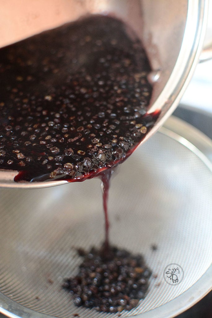 boiled elderberries being poured from a pot to a strainer