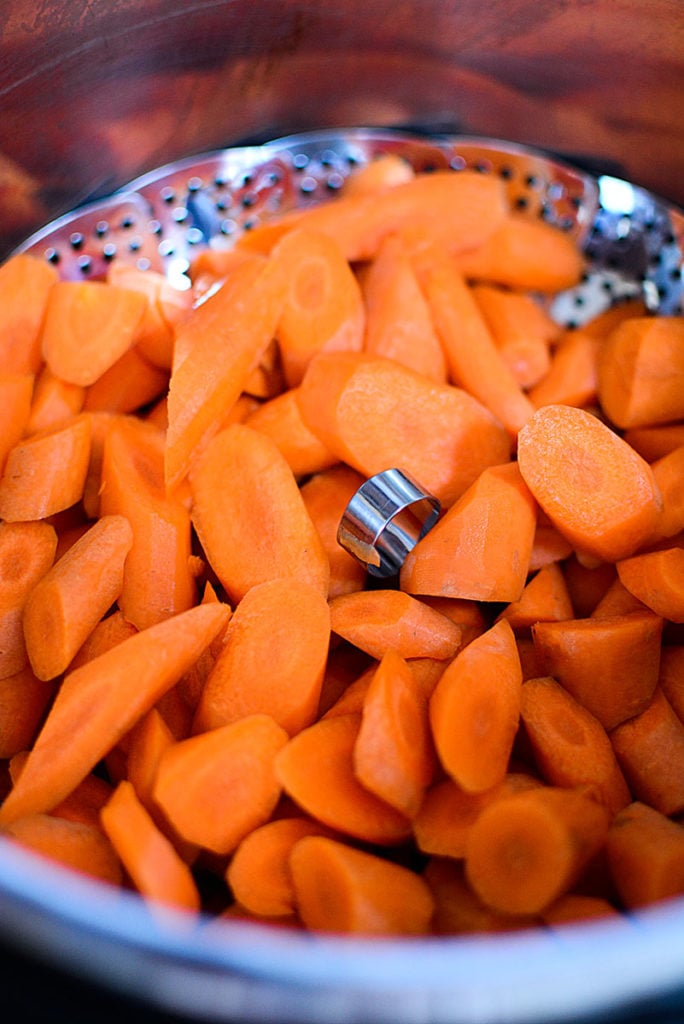 Little pieces of cut fresh carrots on a stainless strainer with handle inside a deep pot