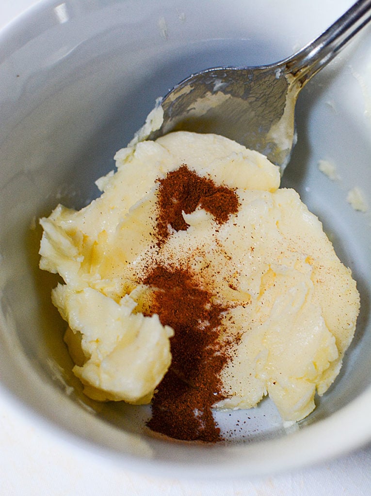 Some softened butter topped with cinnamon on a bowl with spoon