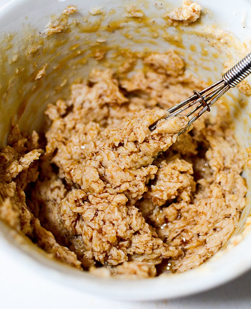 A close up image of butter, maple syrup, and cinnamon mixture being mixed with an egg beater in a small white bowl