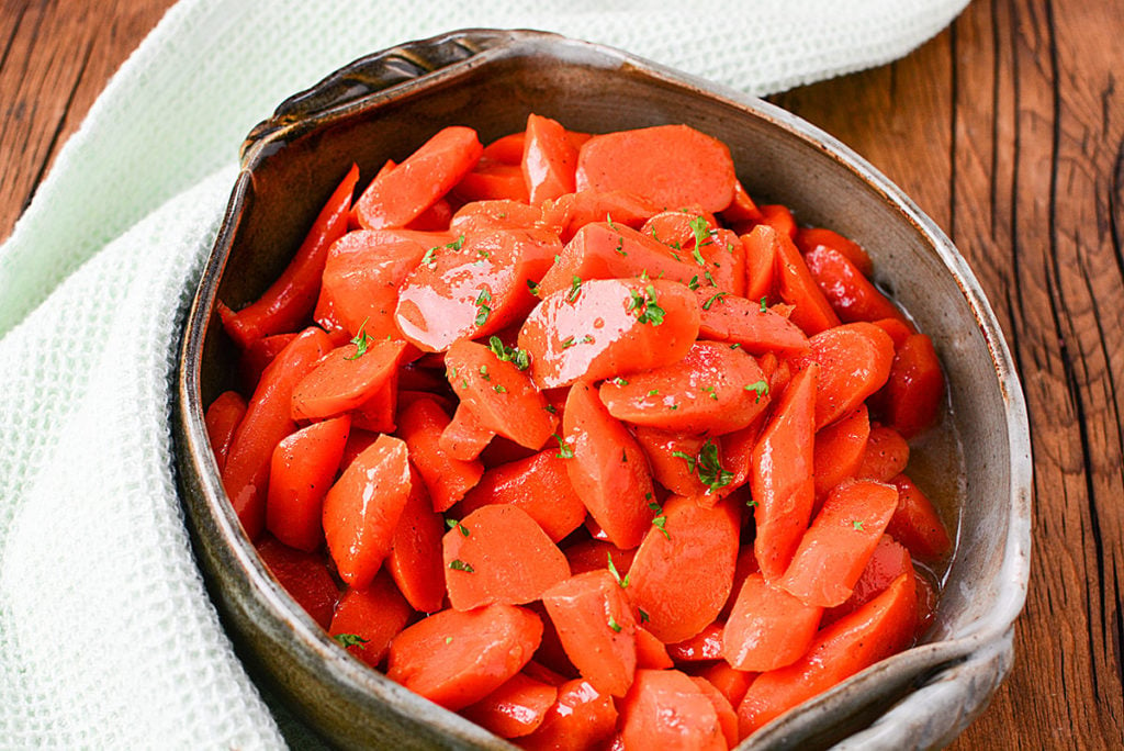 A bowl full of 3 MINUTE MAPLE CINNAMON INSTANT POT CARROTS garnished with some chopped parsley