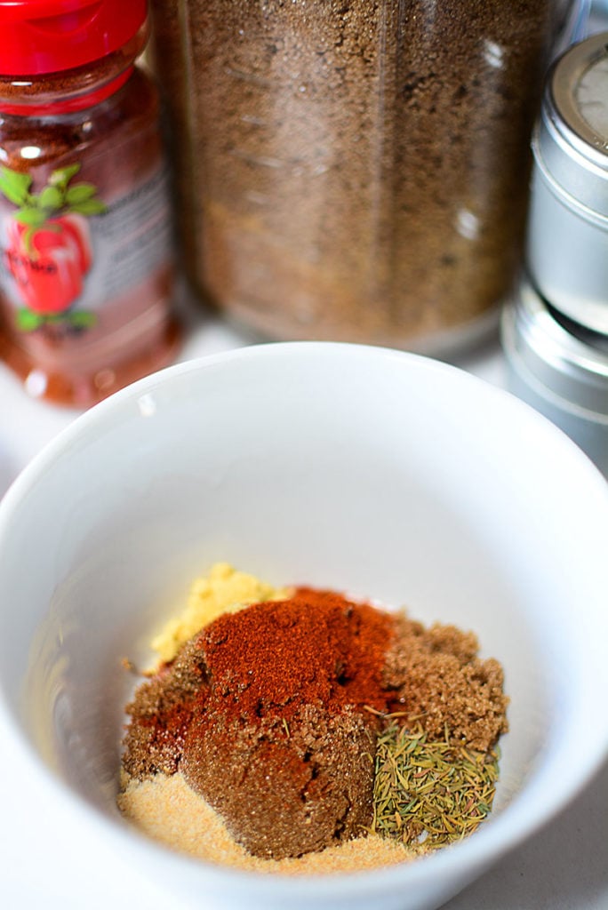 White bowl with 5 seasonings on it. At the background are three containers of three different seasonings