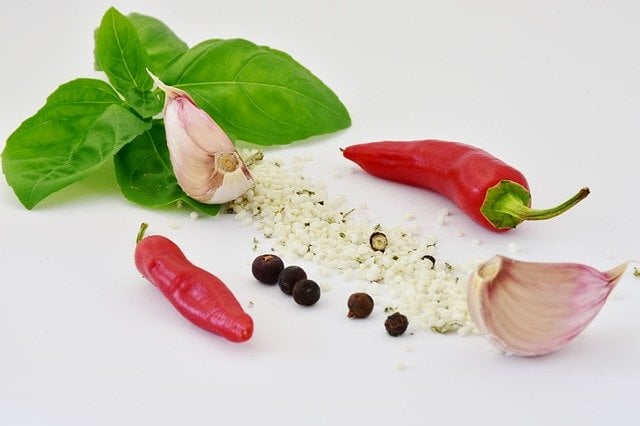 An image of basil leaves, two cloves of garlic, two pieces of red chili pepper, 5 pieces of whole pepper, and some rock salt