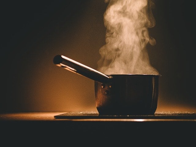 An image of a pot with a long handle on top of a stove. The liquid in the pot is steaming, you can see the smoke coming out of the pot