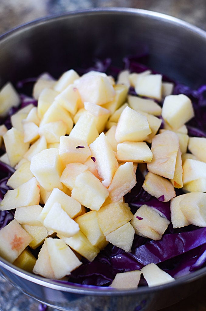 A close up image of stainless bowl with chopped cabbage and diced apples.