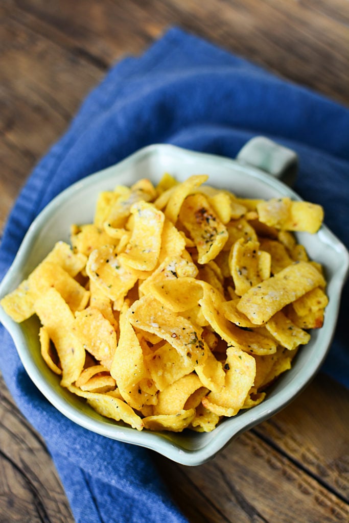 Buttery ranch corn chips on a bowl topped with salt, pepper, and other seasonings. The bowl is sitting on a piece of blue cloth.