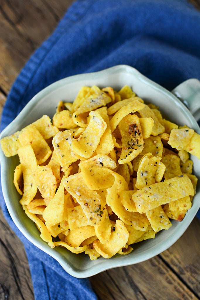 Buttery ranch corn chips on a bowl topped with salt, pepper, and other seasonings. The bowl is sitting on a piece of blue cloth.