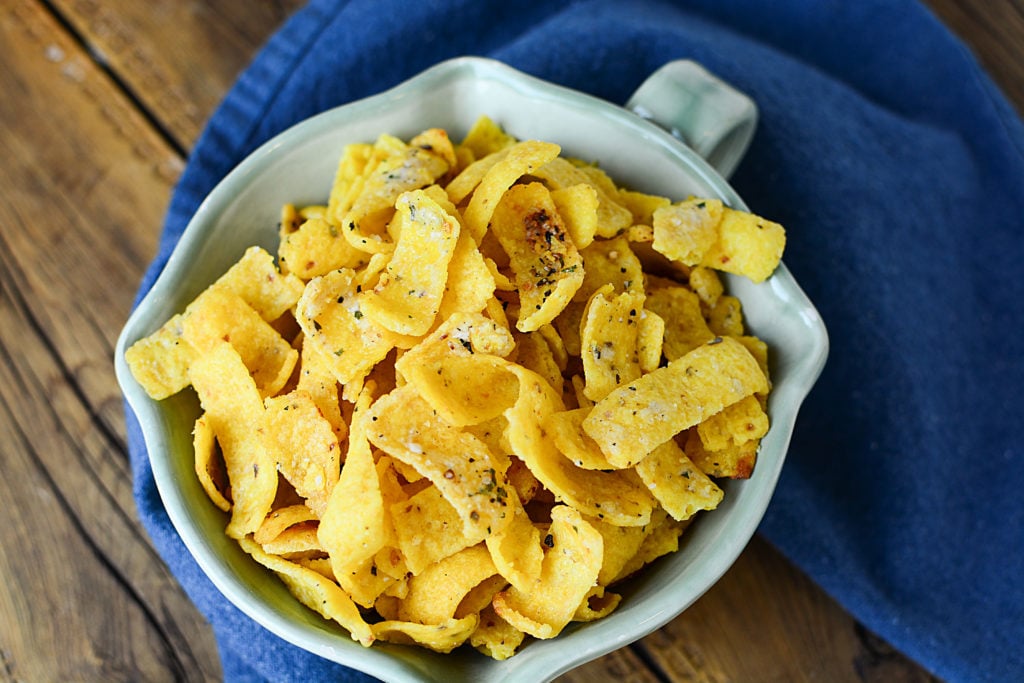 Buttery ranch corn chips on a bowl topped with salt, pepper, and other seasonings. The bowl is sitting on a piece of blue cloth.