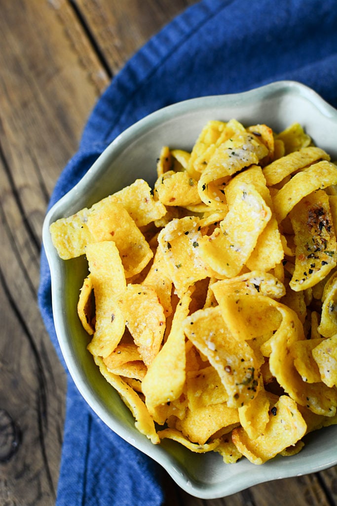 Buttery ranch corn chips on a bowl topped with salt, pepper, and other seasonings. The bowl is sitting on a piece of blue cloth.