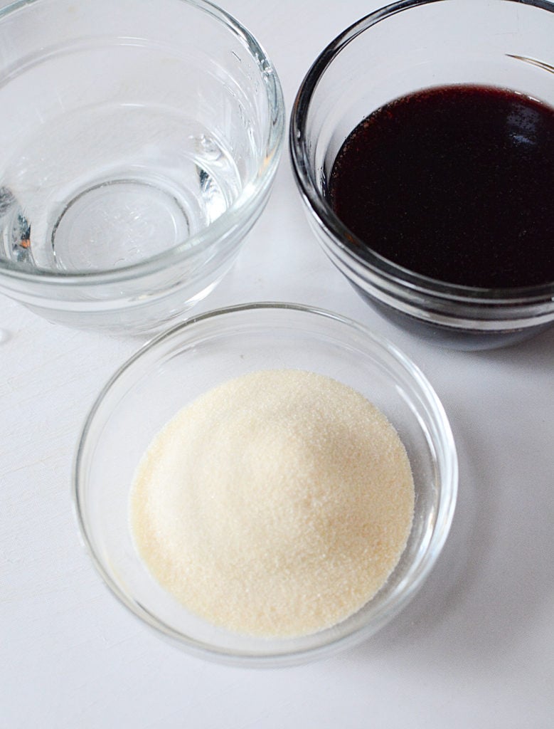 An image of a small bowl of gelatin powder, bowl of warm water, and a small bowl of elderberry syrup