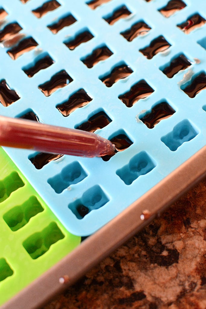 Elderberry syrup being poured one by one to gummy bear shaped mold using a dropper