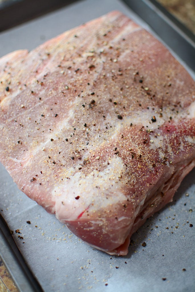 A piece of fresh pork laid out on a baking pan seasoned with salt and pepper on top