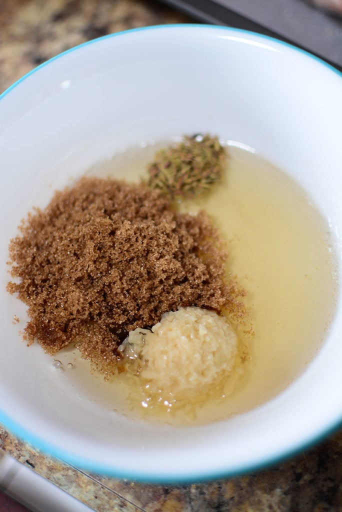 A small white bowl with some brown sugar, dried thyme, grated ginger, and oil