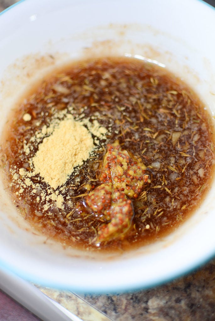 A small white bowl with some brown sugar, dried thyme, grated ginger, oil, honey, mustard powder. and seedy mustard.