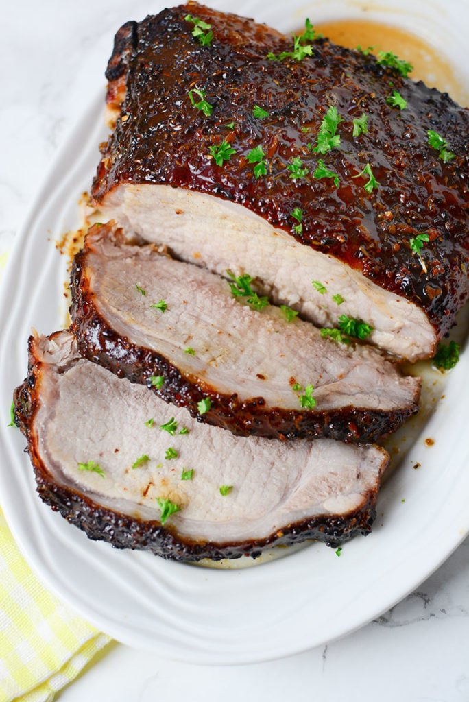 An image of honey mustard glazed piece of pork garnished with some chopped parsley. Meat if sitting on a white platter. 