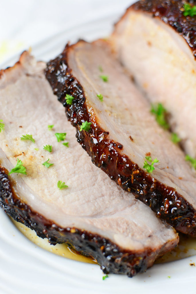 A close up image of honey mustard glazed piece of pork garnished with some chopped parsley. Meat if sitting on a white platter. 