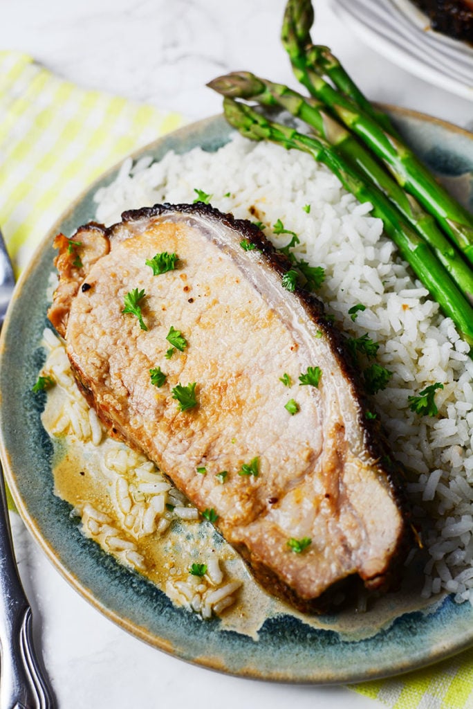 An image of a piece of honey mustard glazed port on top of steamed rice with some asparagus on the side, served on a blue plate.