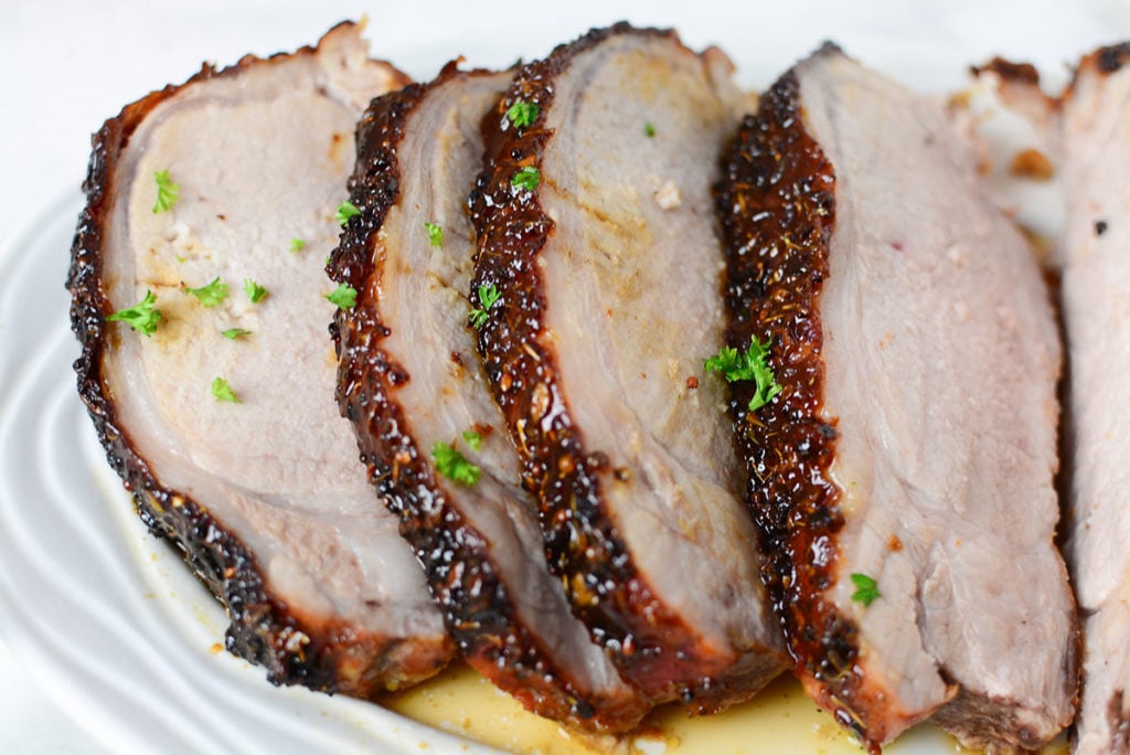 A close up image of honey mustard glazed piece of pork garnished with some chopped parsley. Meat if sitting on a white platter. 