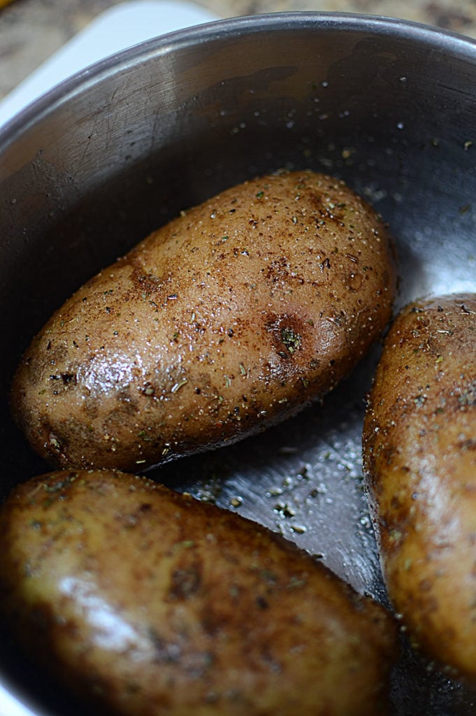 Three pieces of big fresh potatoes in an empty pot, rubbed with some oil, pepper, and Italian seasoning.