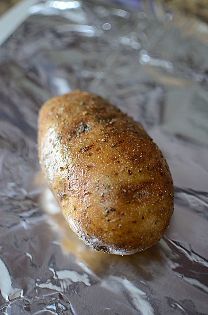 A piece of big fresh potato sitting on a foil and rubbed with some oil, pepper, and Italian seasoning.