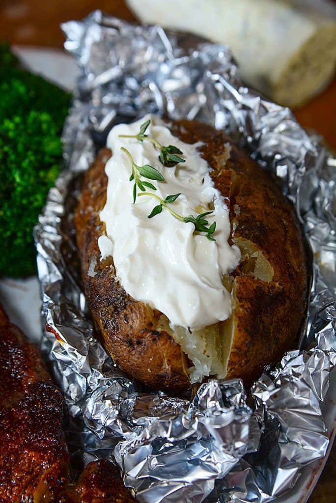 A close up image of crock pot baked potato sitting on foil and topped with some mayo garnished with some fresh herbs. 