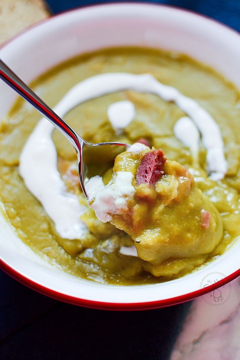 Split pea soup in a bowl with a spoonful of the soup above it.