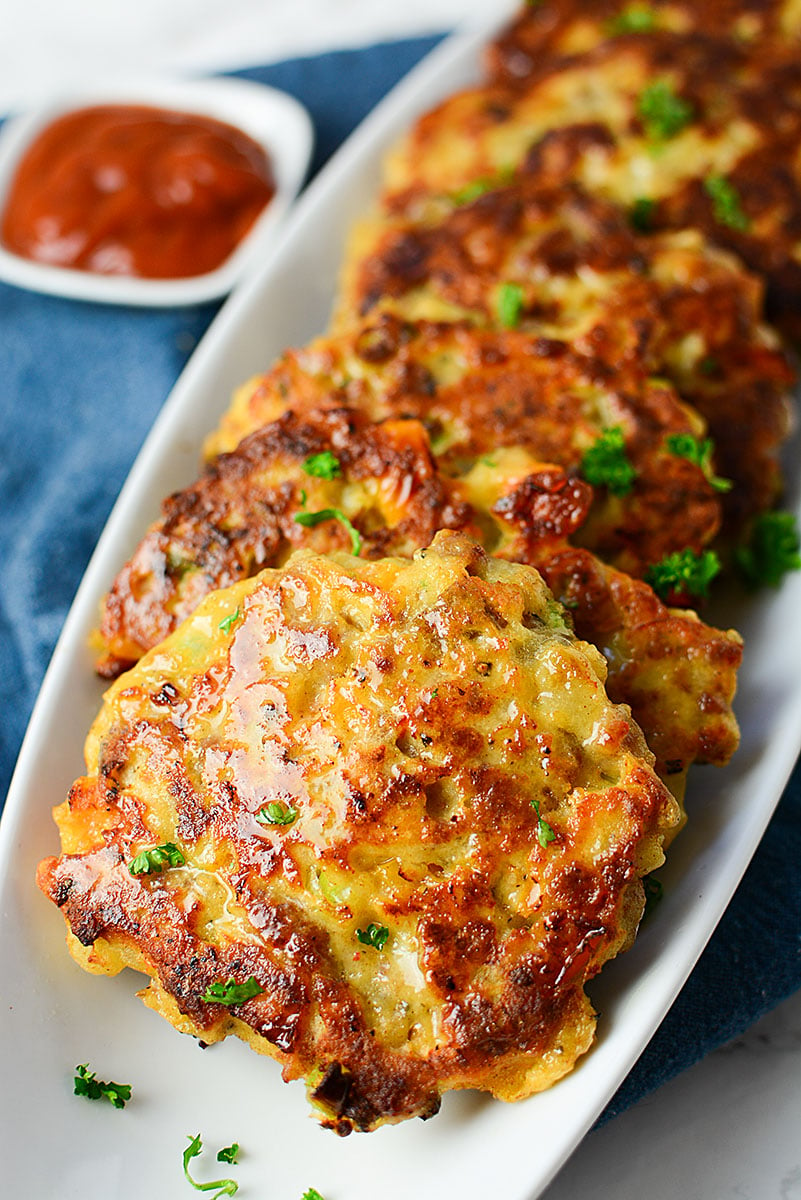 Sausage and potato patties lined up laying on a white serving dish with ketchup in the background.