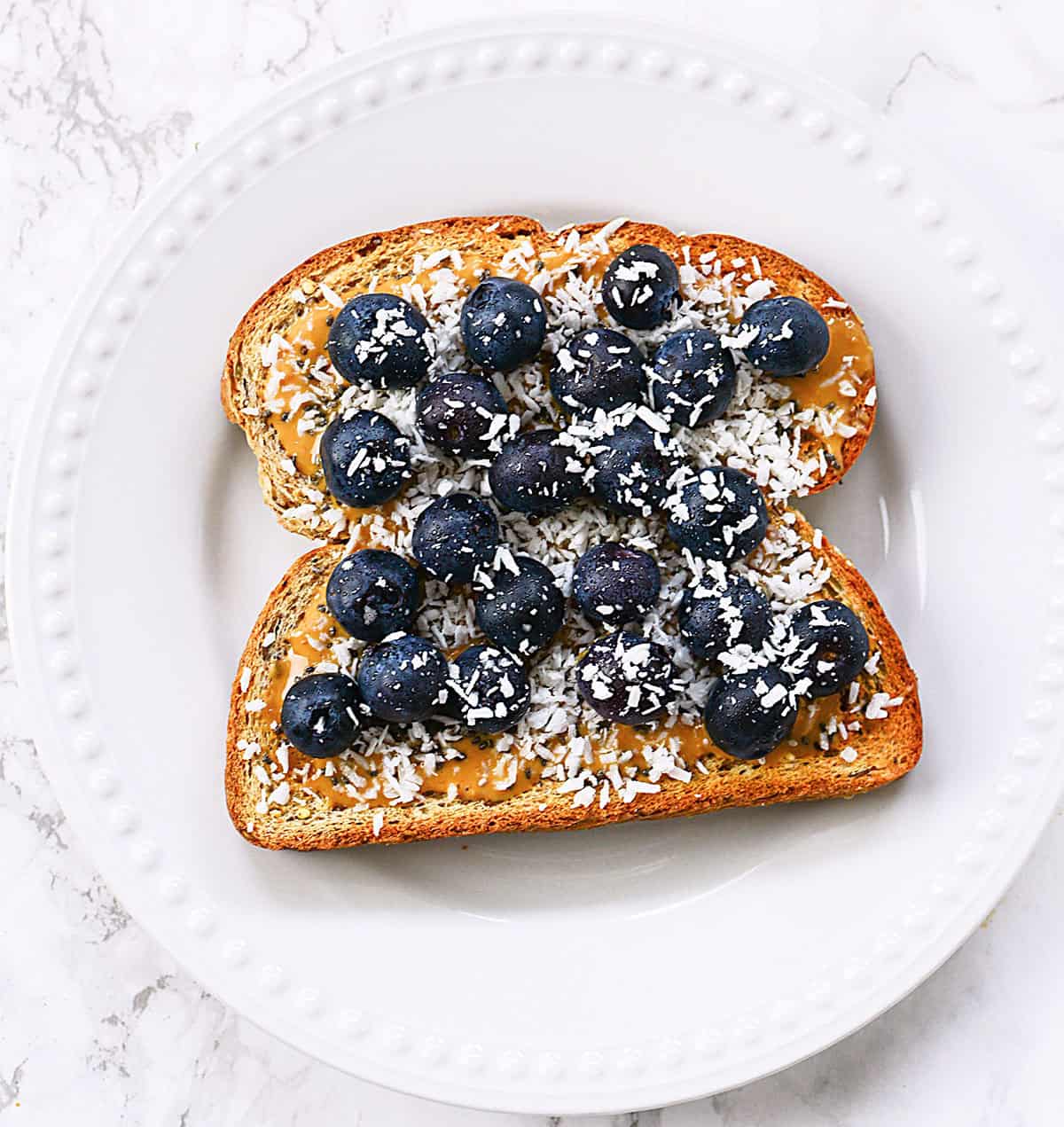 Toast with blueberries, peanut butter and coconut on a white plate.