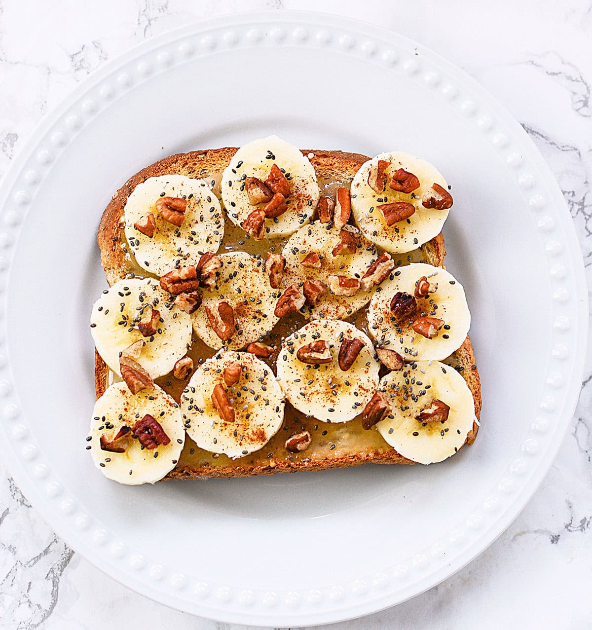 Toast with honey, bananas and pecans sitting on a white plate.