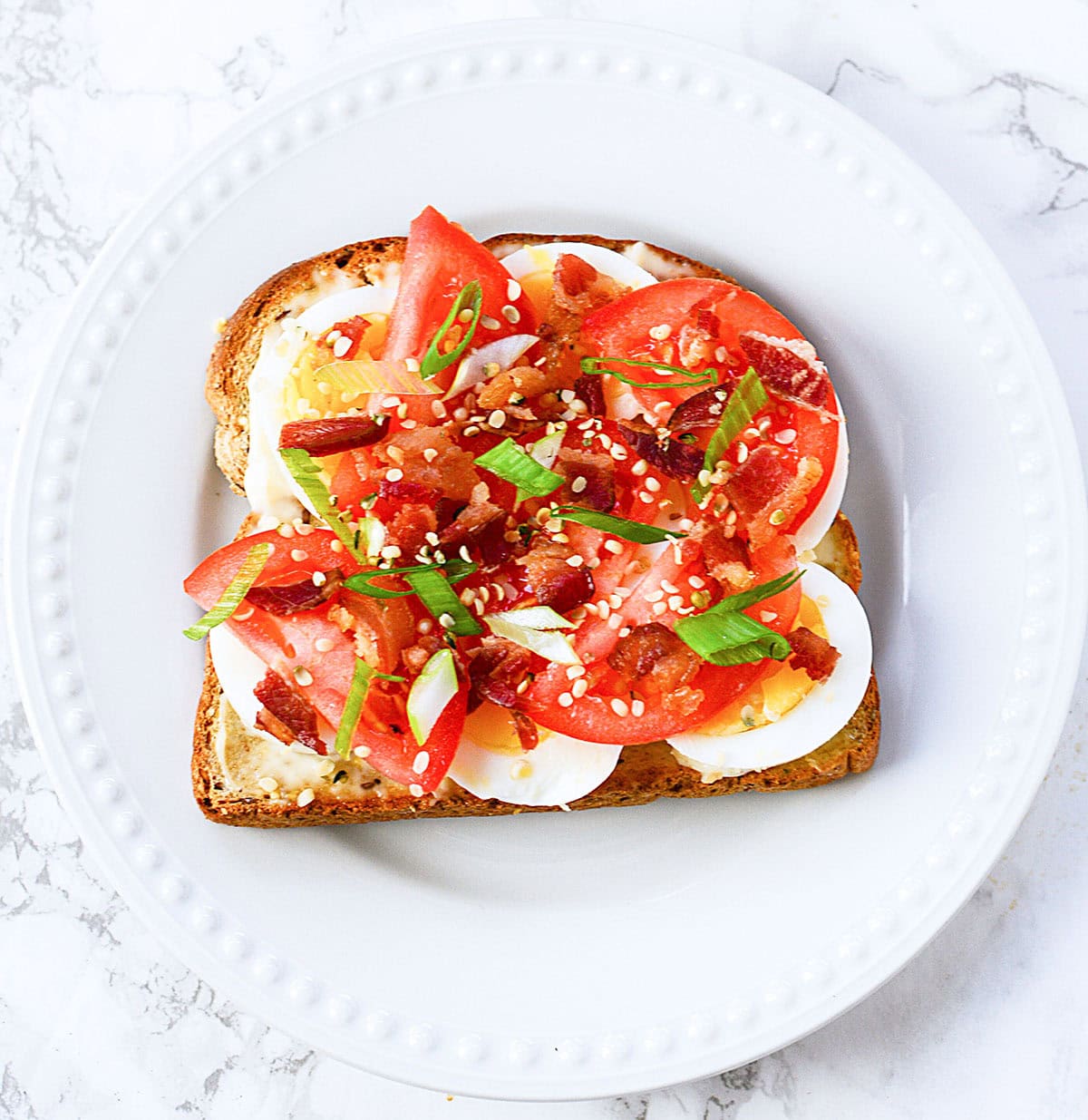 Bacon, tomato and egg on toast on a white plate.