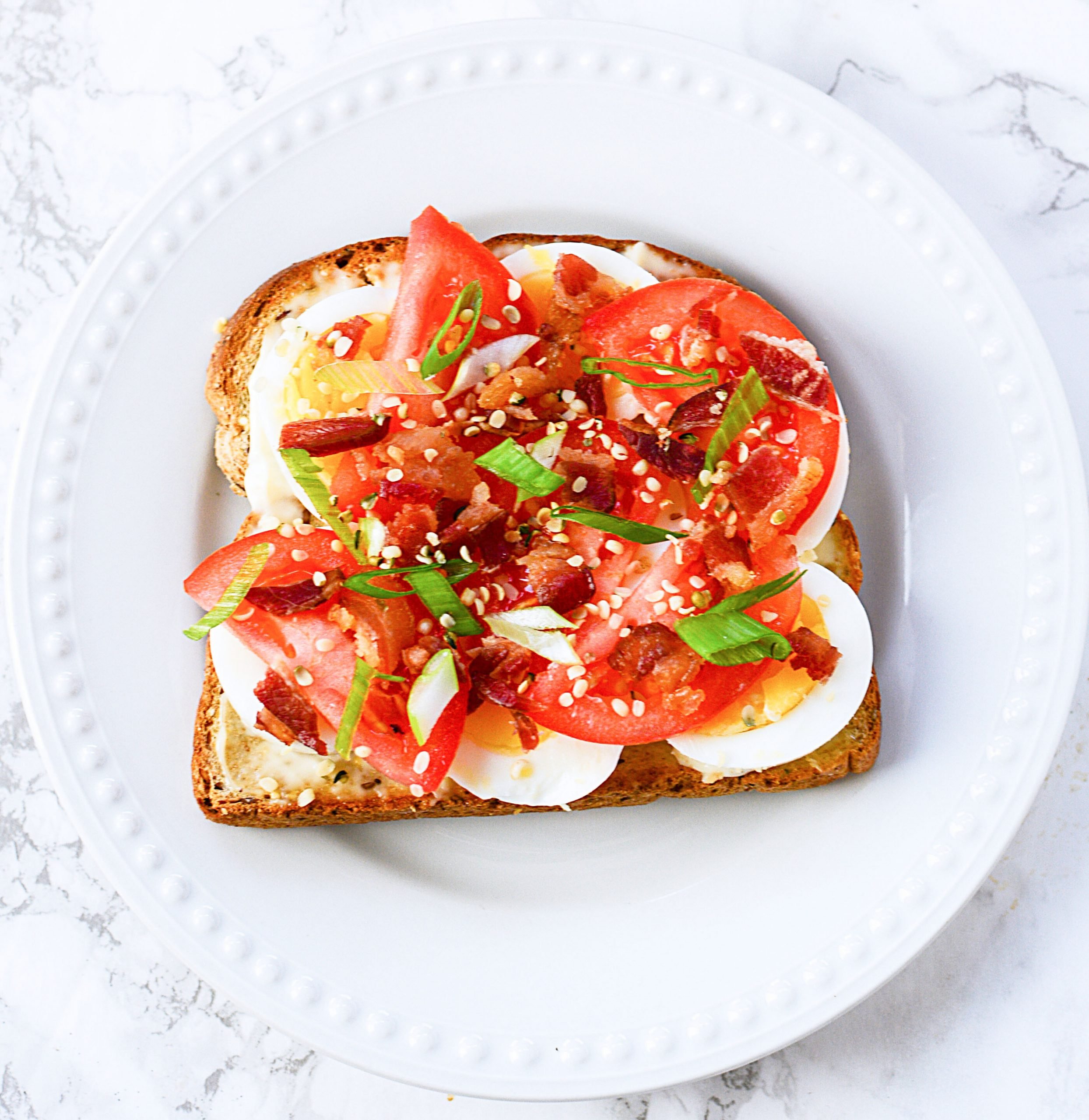 Toast with mayo, hardboiled egg, sliced tomato and bacon bits over the top.