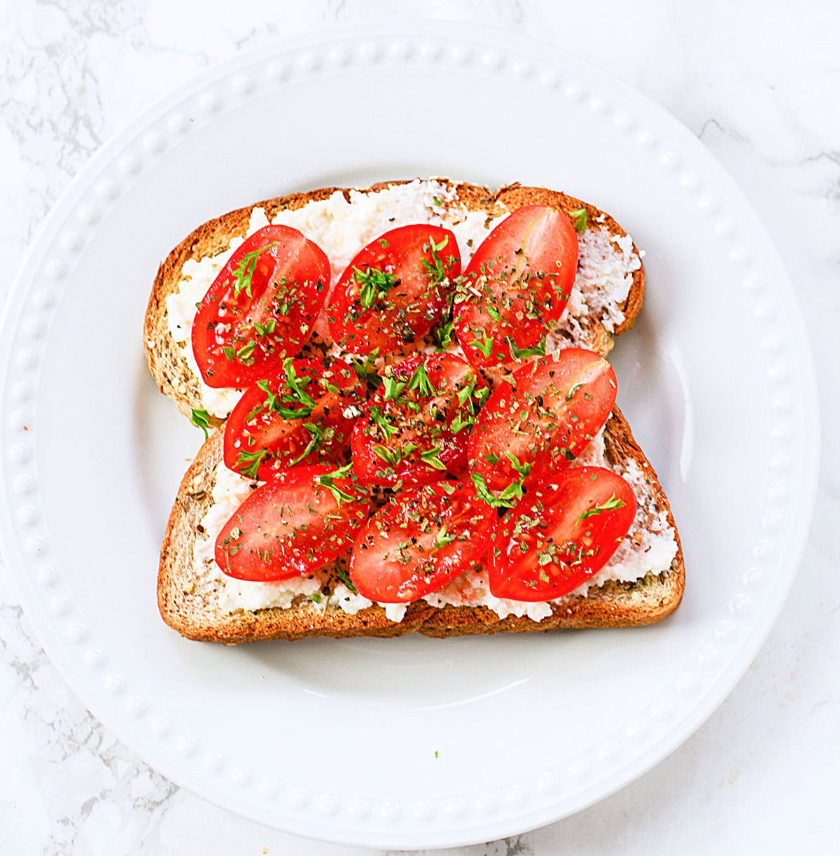Tomatoes with ricotta cheese on toast on a white plate.