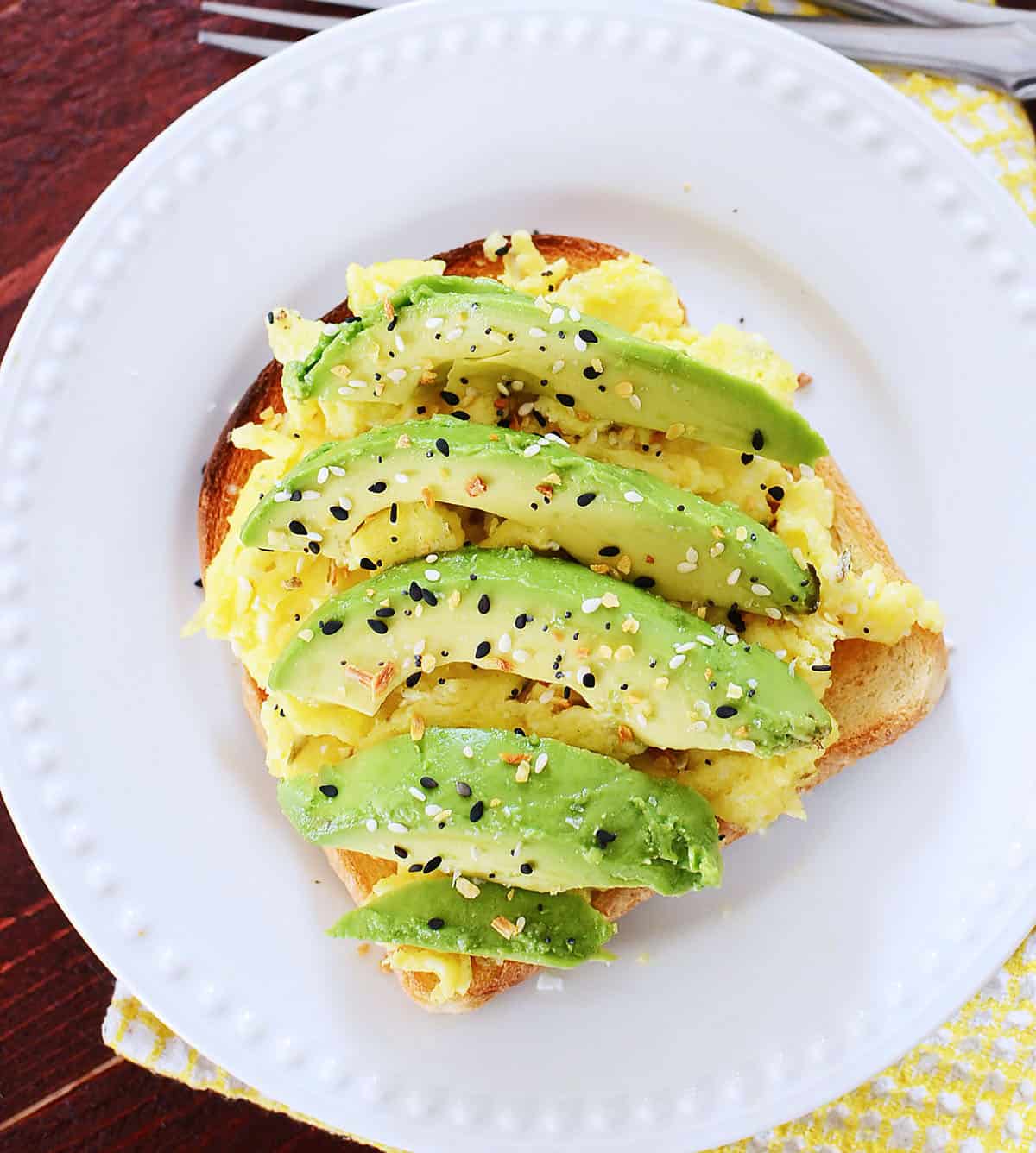 Scrambled eggs and avocado on toast on a white plate.