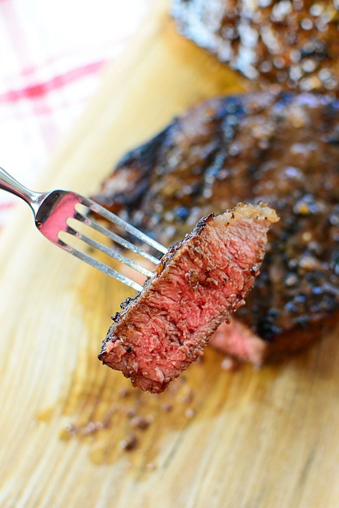 A fork holding a bite of perfectly cooked steak to medium rare doneness.