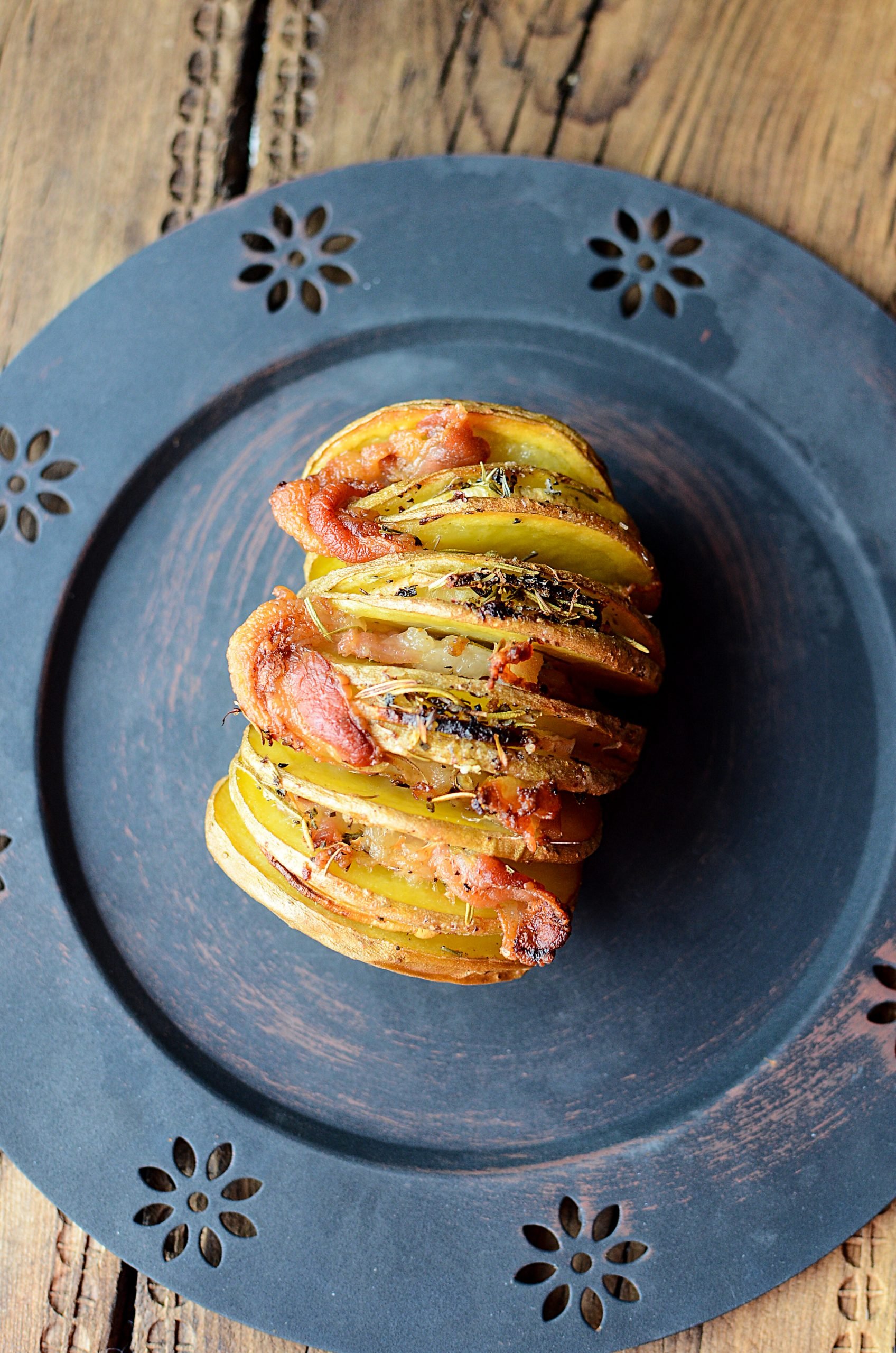 A potato with bacon and onion on a black plate.