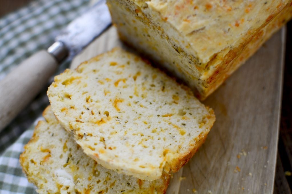 Cheddar and dill bread sitting on a wood board with a few slices laying in front of the loaf.