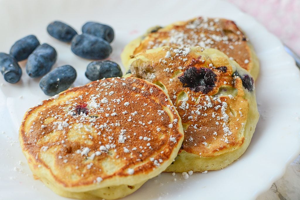 Honey berries on a plate next to three toddler sized pancakes