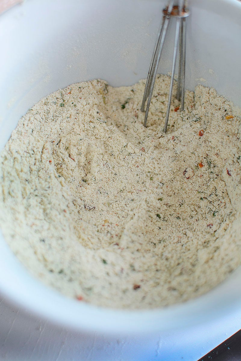 All the seasoning packets required for this recipe are mixed together in a white bowl. A whisk sits in the seasoning powder.