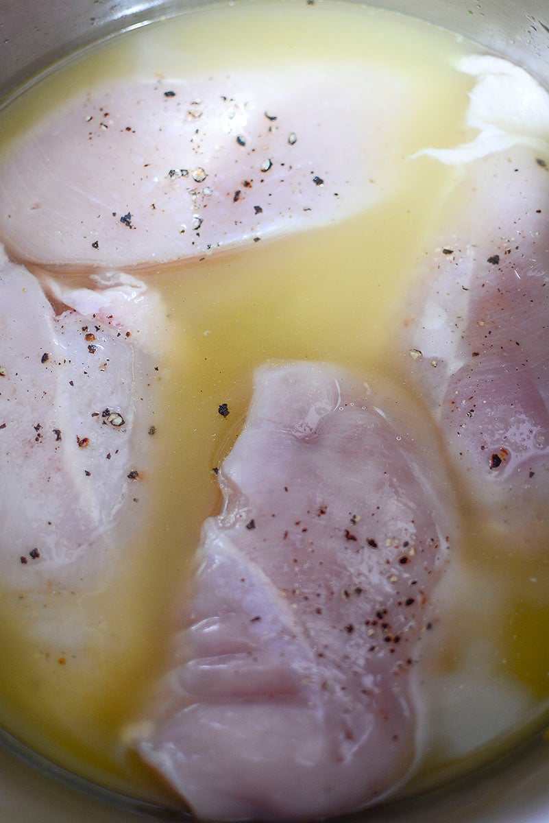 Four seasoned chicken breasts sitting in chicken broth in the instant pot cooking liner.