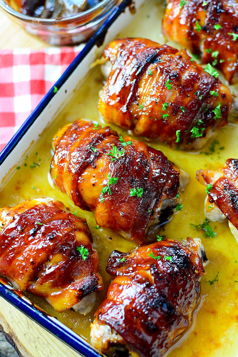 5 bacon wrapped chicken thighs in a roasting pan on a red and white checkered napkin. 