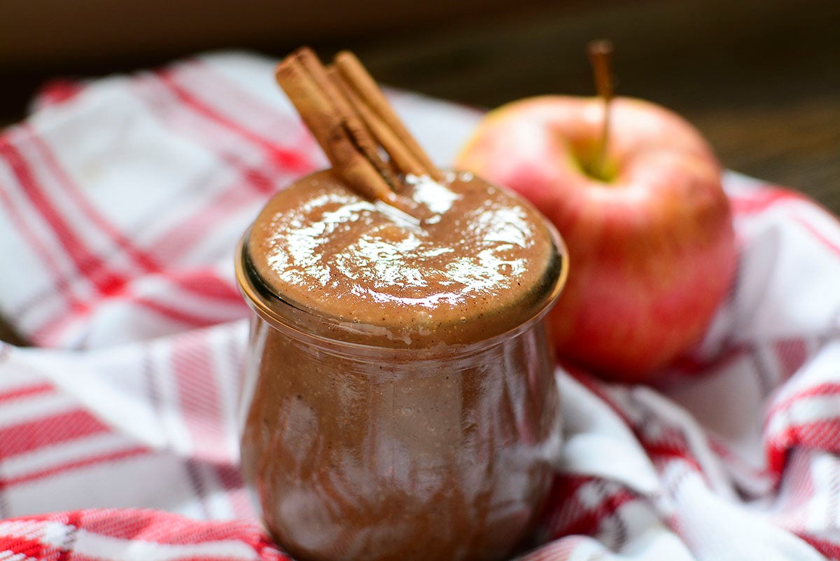 Apple butter in a glass jar on a red checked tea towel. 