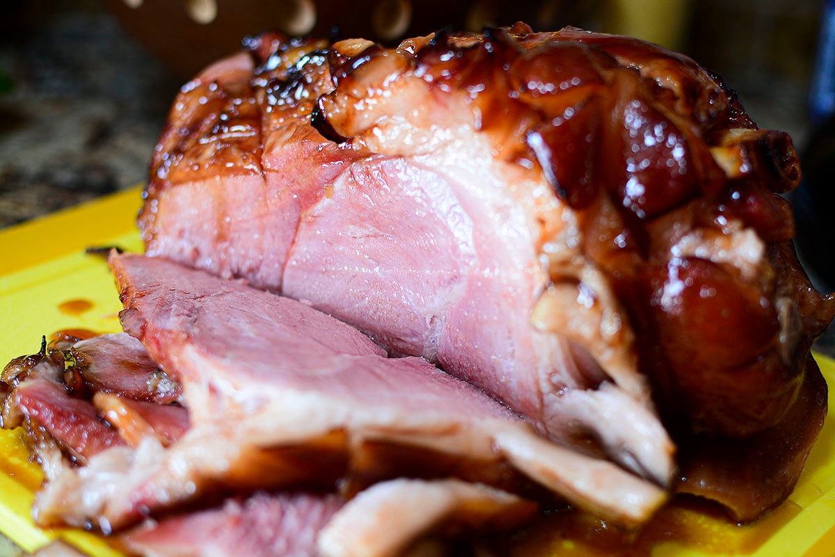 A ham with apricot glaze showing a few slices cut on a cutting board.