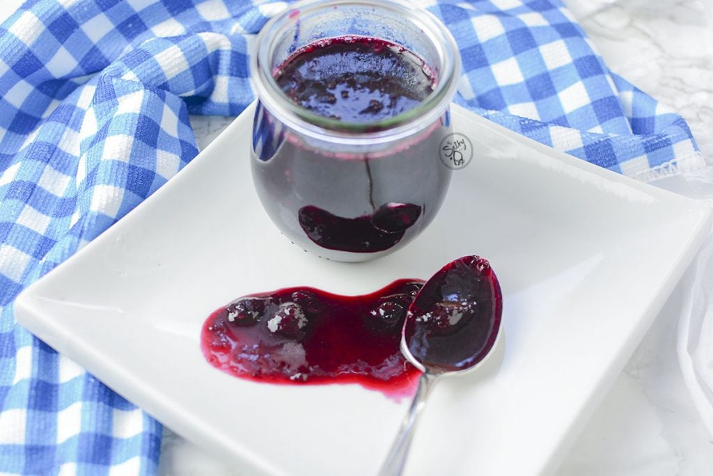 keto blueberry sauce looking so pretty on a white plate and a blue checkered napkin.