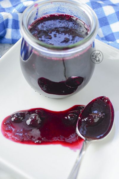 keto blueberry sauce looking so pretty on a white plate and a blue checkered napkin.