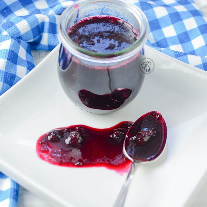 keto blueberry sauce looking so pretty on a white plate and a blue checkered napkin.