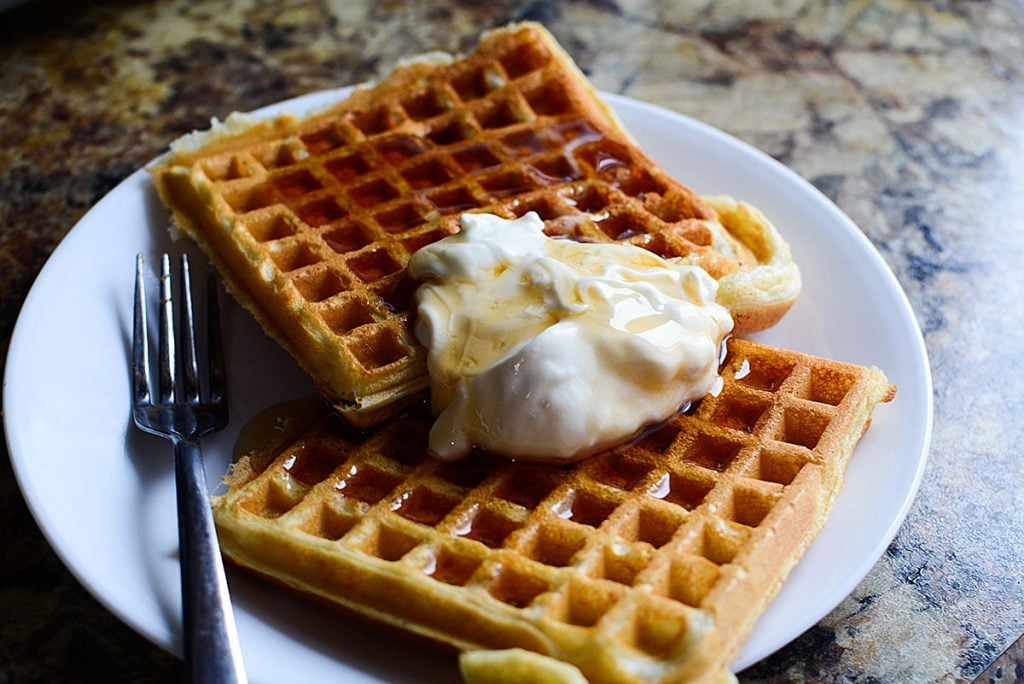 A closeup photo of the fluffy buttermilk waffles with creme fraiche and warm syrup on top!