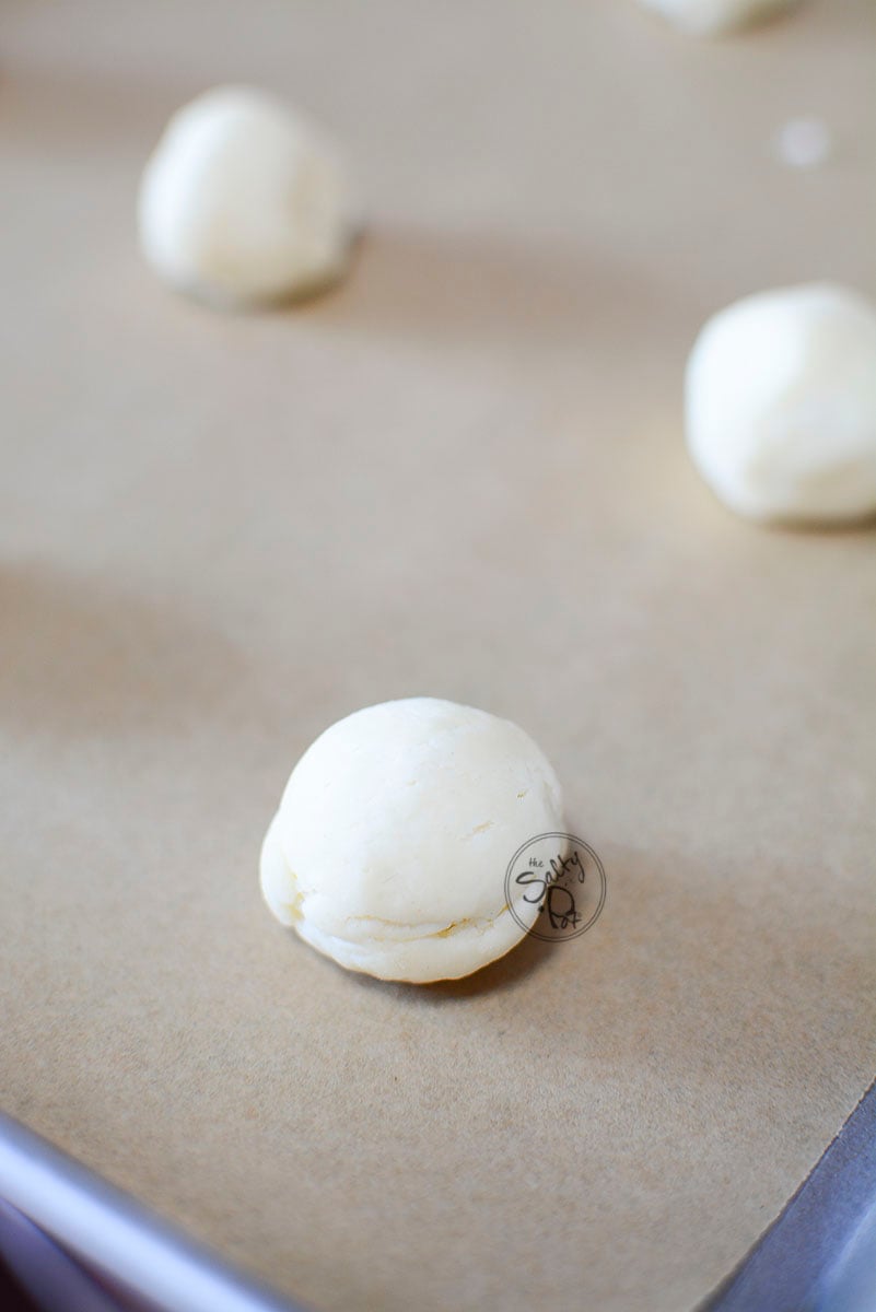 Round balls of shortbread cookie dough on a parchment lined baking sheet.
